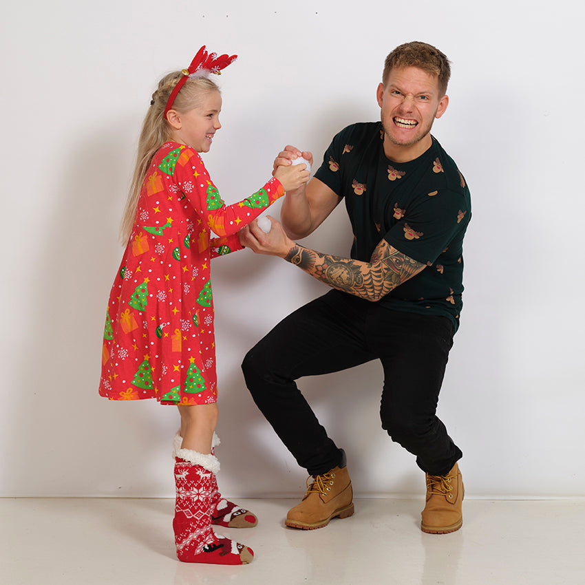 Ett barn i röd julklänning med julgranar poserar med en man.